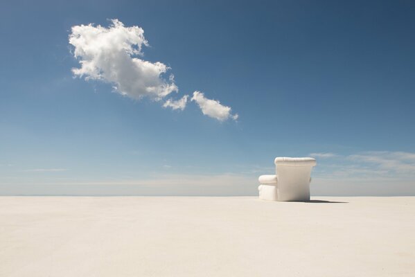 A white armchair stands alone in the desert under a blue sky