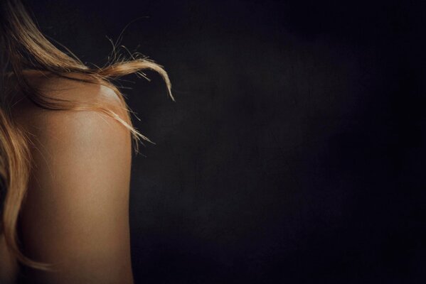 Blonde curls on the shoulder of a young girl. Dark background