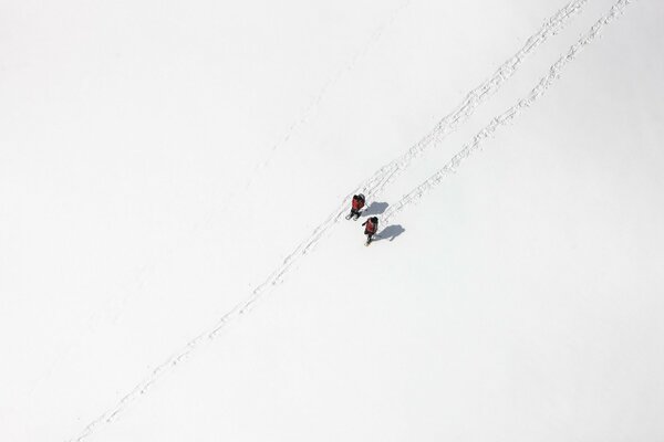 A picture from a height, a white field in the snow, two people walking along the trail