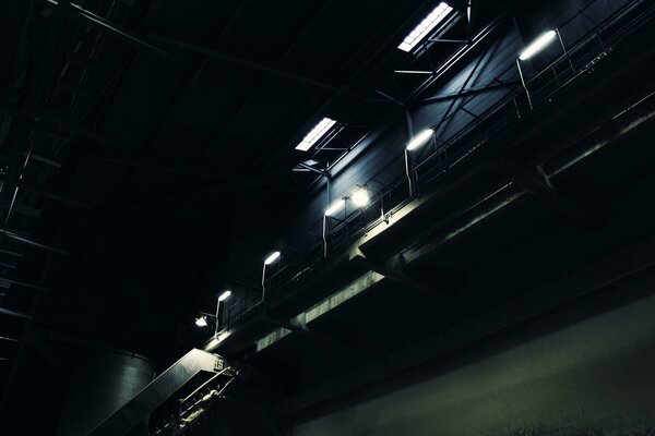 L entrepôt est sombre. L escalier est faiblement éclairé par des lanternes