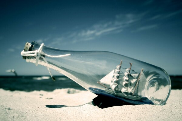 Eine Flasche mit einem Segelboot im Inneren liegt im Sand