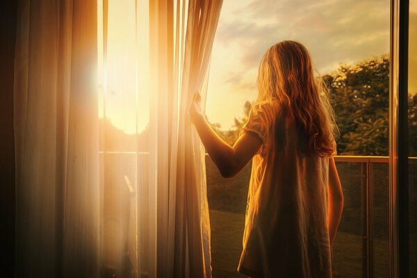 La niña Mira la puesta de sol a través de la ventana