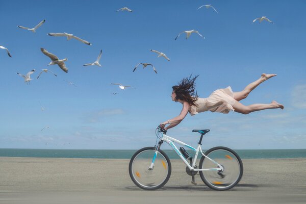 Una niña vuela sobre una bicicleta en la orilla del mar con gaviotas