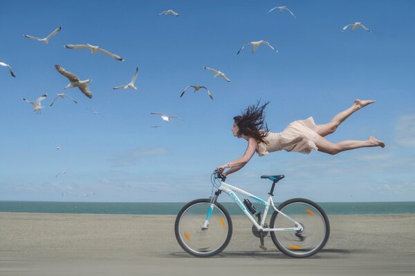 La jeune fille vole au-dessus de la moto sur le bord de la mer avec les mouettes