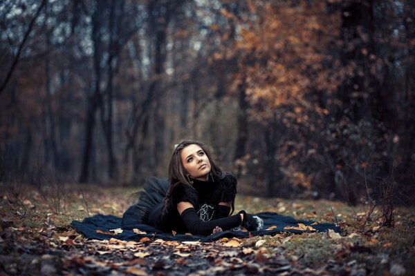 Chica acostada en las hojas en el bosque de otoño