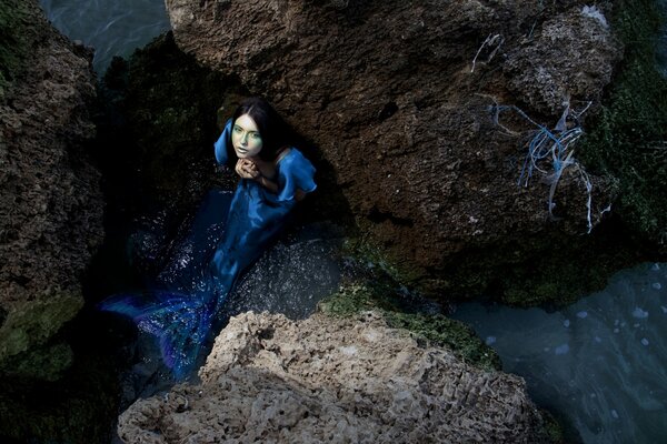 Sirena azul en las piedras, sentada en el agua