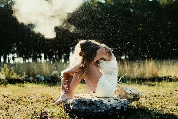 A girl in white is sitting on a stone