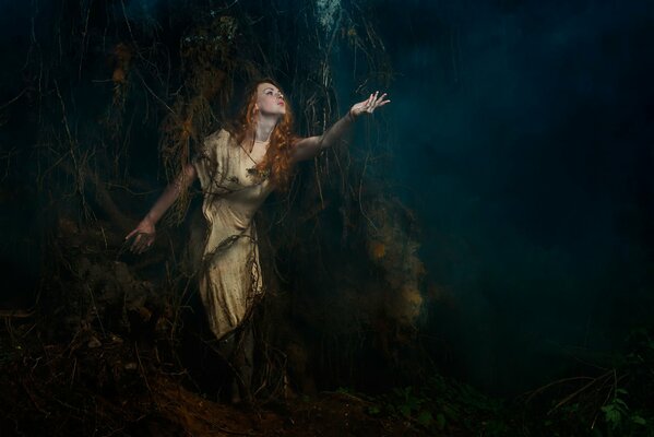 Una chica en las raíces de un árbol Mira el bosque de niebla