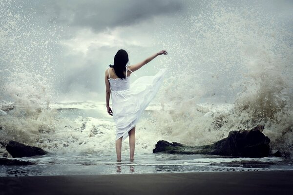 Ein Mädchen im weißen Kleid steht am Meer