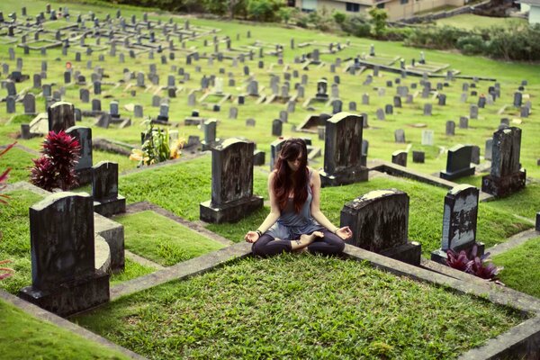 A girl in the lotus position in a green cemetery