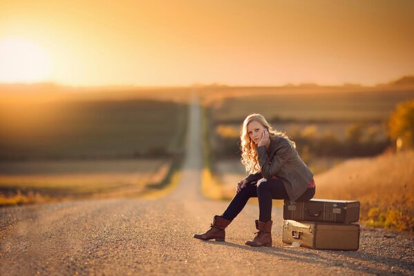 A girl is sitting on suitcases on the road