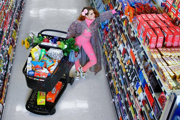 The girl at the shelves of the store with a cart