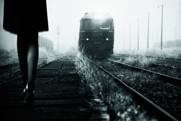 BW foto delle gambe di una ragazza di fronte a un treno in avvicinamento