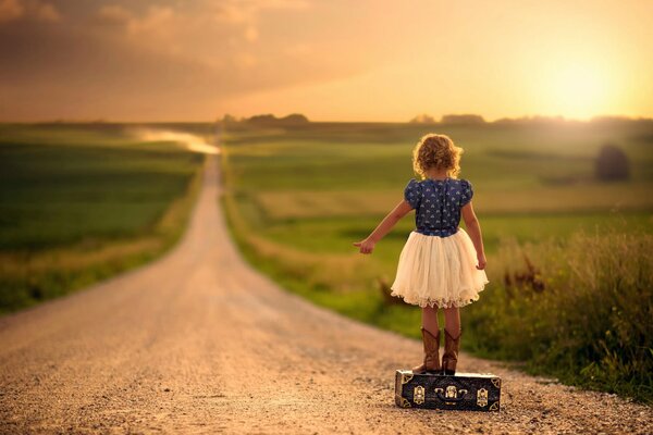 Ragazza in piedi sulla valigia sulla strada