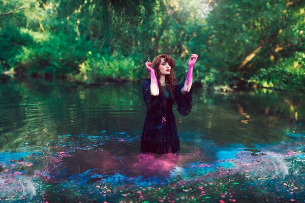 Servizio fotografico di una ragazza in un vestito scuro e con vernice sulle mani in acqua