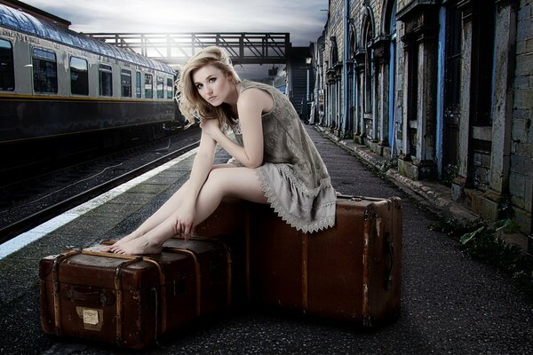 Une jeune femme est assise sur une valise à la main et attend un train