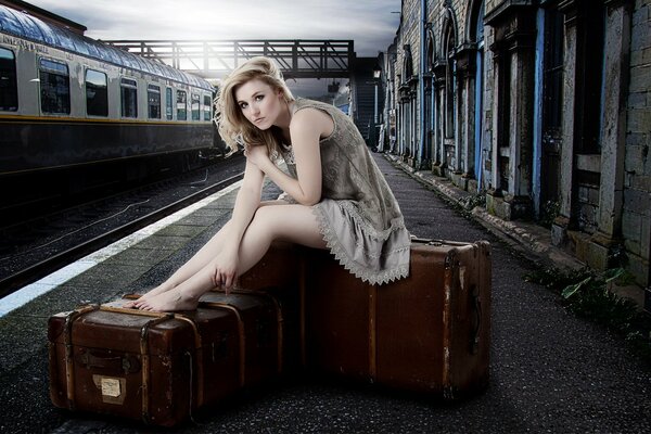 Dziewczyna siedzi na walizkach i czeka na pociąg