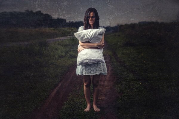 A girl with a pillow in an empty field