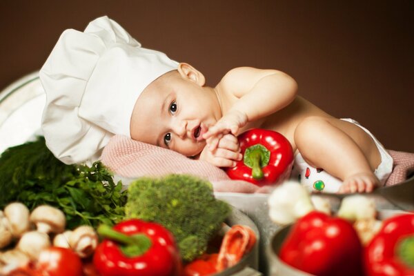 Un bébé dans un поворском d un bonnet de nuit parmi les légumes