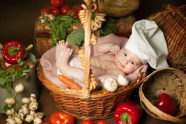 Un jeune dans le bonnet de cuisinier se trouve dans le panier de légumes