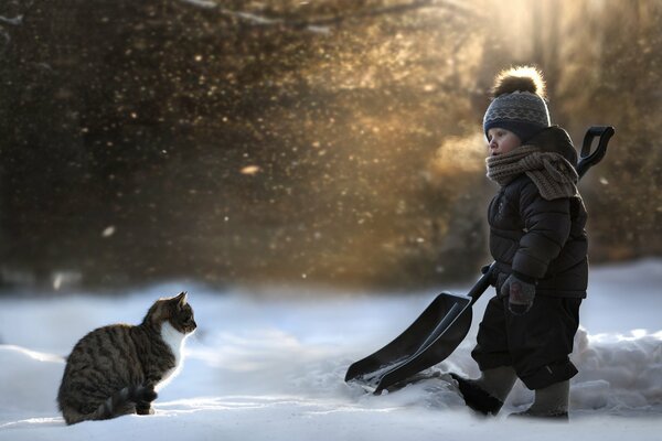 Il bambino con il gatto è uscito per rimuovere la neve