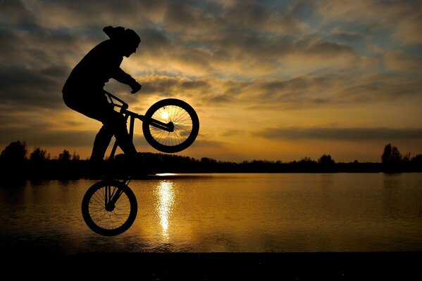 Hombre en bicicleta al atardecer en un salto junto al lago