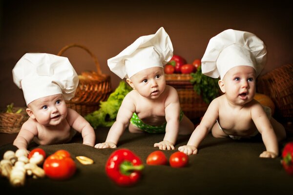 Niños pequeños en tapas de cocina entre verduras y cestas
