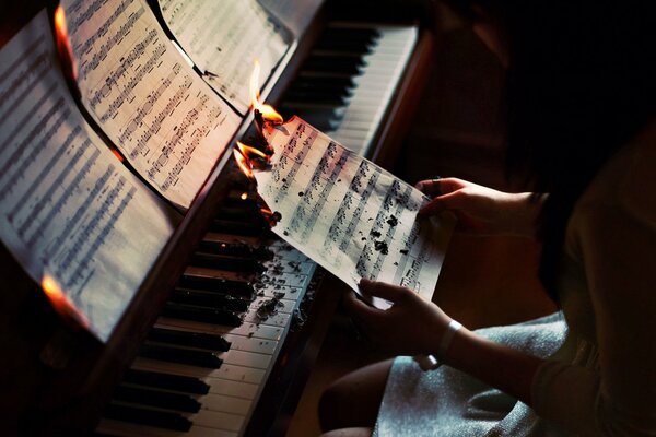 La jeune fille est assise derrière le piano et brûle une feuille avec des notes