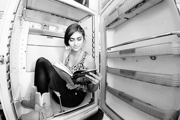 Хрупка девушка сидит в холодильнике и читает книгу