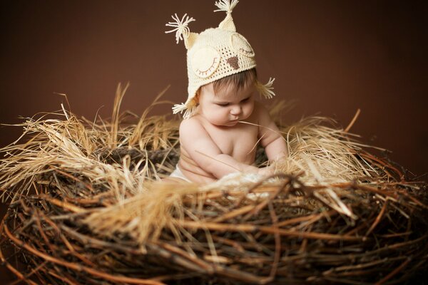 A baby with an owl hat is sitting in a nest