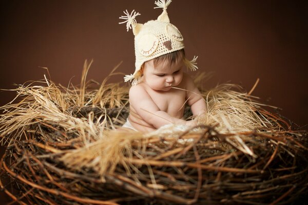 Un enfant avec un bonnet de hibou est assis dans le nid