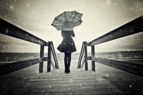Una niña se encuentra en un puente bajo la nieve con un paraguas en sus manos
