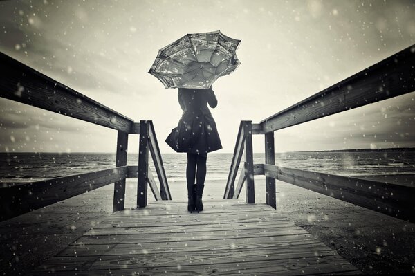 Ragazza in piedi su un ponte sotto la neve con un ombrello in mano