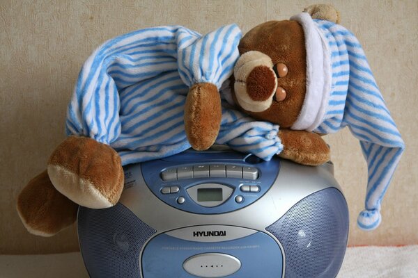 A teddy bear in pajamas is lying on a tape recorder