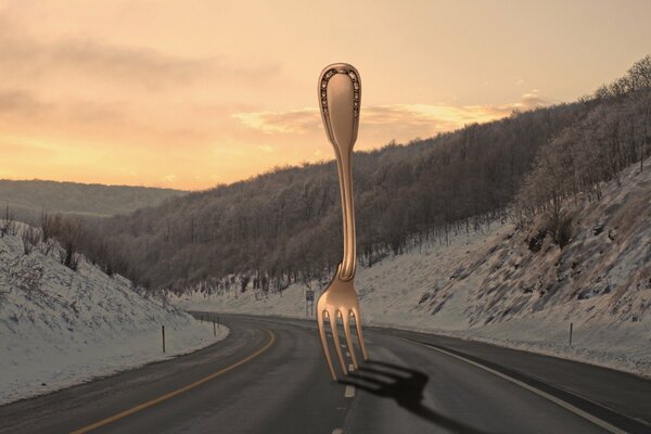 A silver fork in the middle of a road and a snowy forest