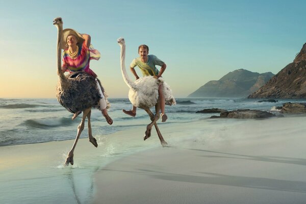 A man and a woman ride an ostrich along the shore