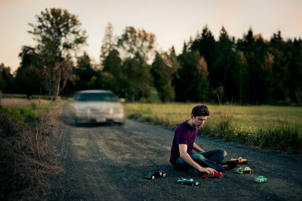 El chico se sienta en la carretera y juega con los coches
