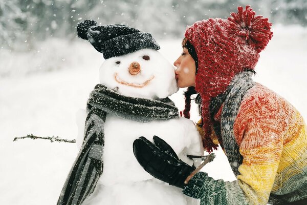 Das Mädchen küsst den Schneemann, den sie im Winter aus dem Schnee geblendet hat