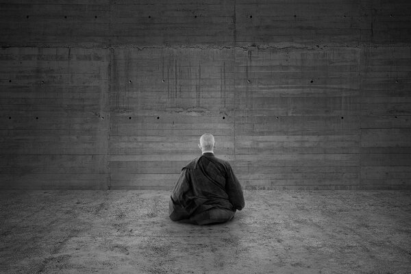A black and white monk meditates against the wall