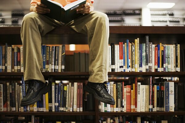 L homme est assis sur une étagère dans la bibliothèque et lit