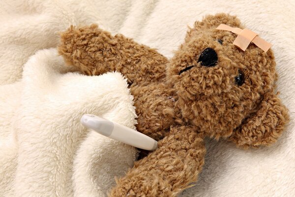 Teddy bear with a thermometer in bed