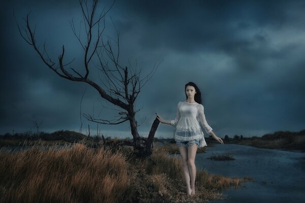 Oriental girl walks past a dead tree at night