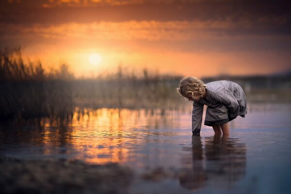 La niña se inclinó hacia el agua en la que se refleja el sol