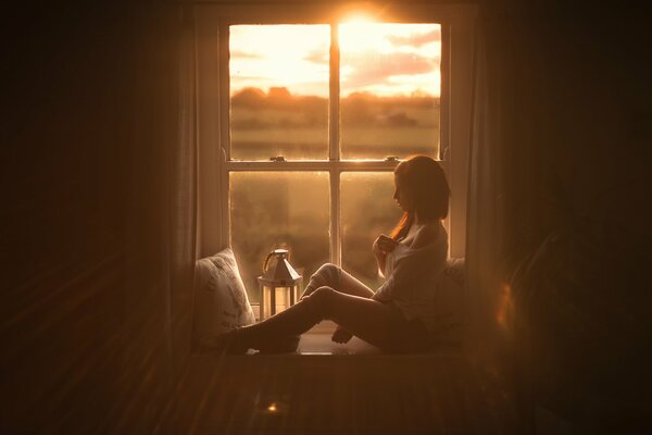 Chica en el alféizar de la ventana en el fondo de la puesta de sol