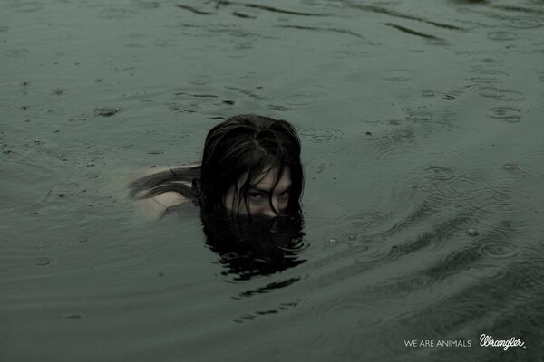 A girl is swimming in a night lake. Only the head sticks out above the water
