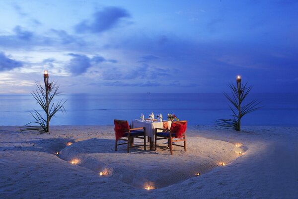 Un tavolo servito con una cena romantica la sera su una spiaggia deserta