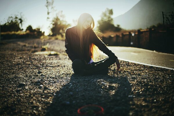 Fille assise sur la route et le soleil joue dans ses cheveux