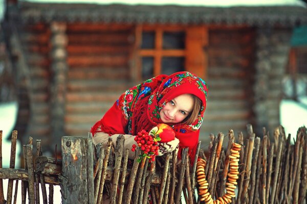 A girl in a Russian scarf with steering wheels on the background of a hut