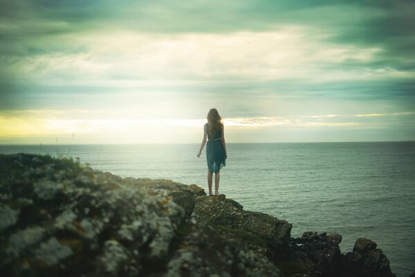 A girl in a dress looks from a cliff