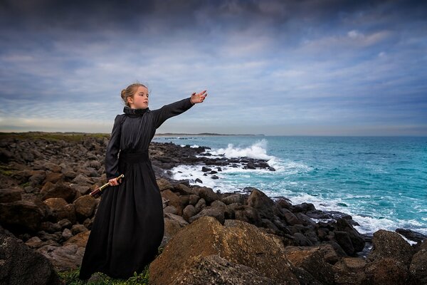 Chica en un vestido oscuro en la orilla rocosa del mar